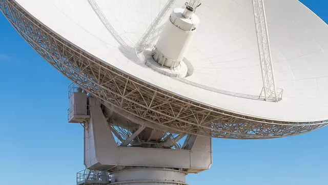 A large deep-space communications antenna stands at a desert research complex in California.